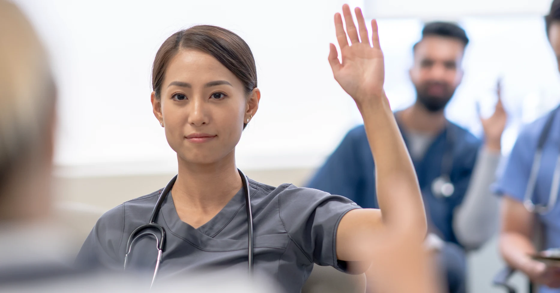Nurse raising hand to ask question in room with other nurses