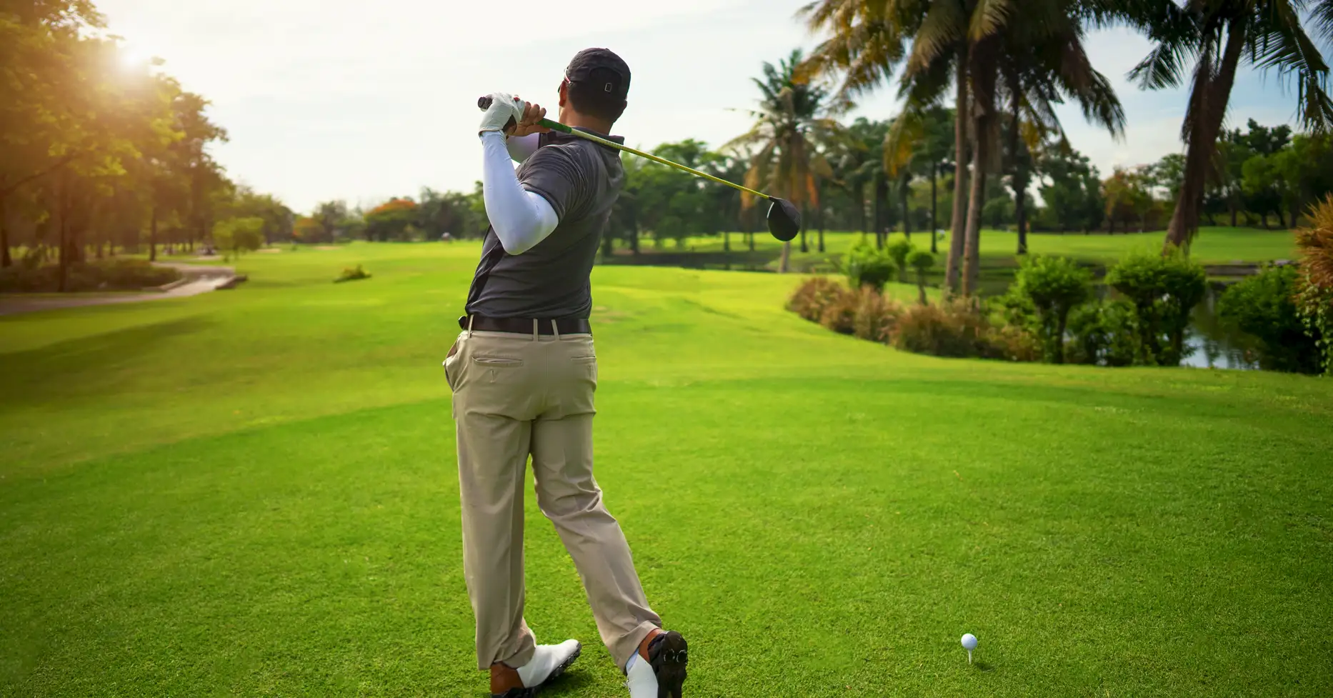 Man taking swing on golf course surrounded by palm trees