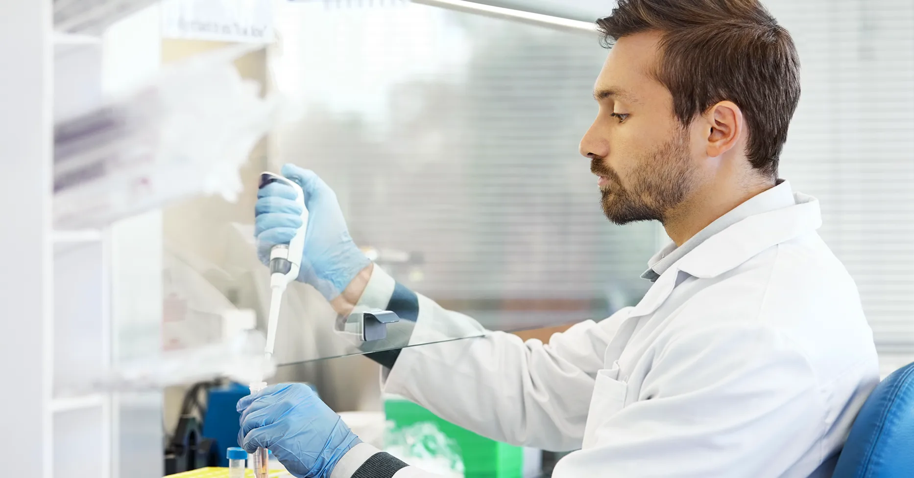 Gloved man in lab coat adding liquid to test tub in medical lab