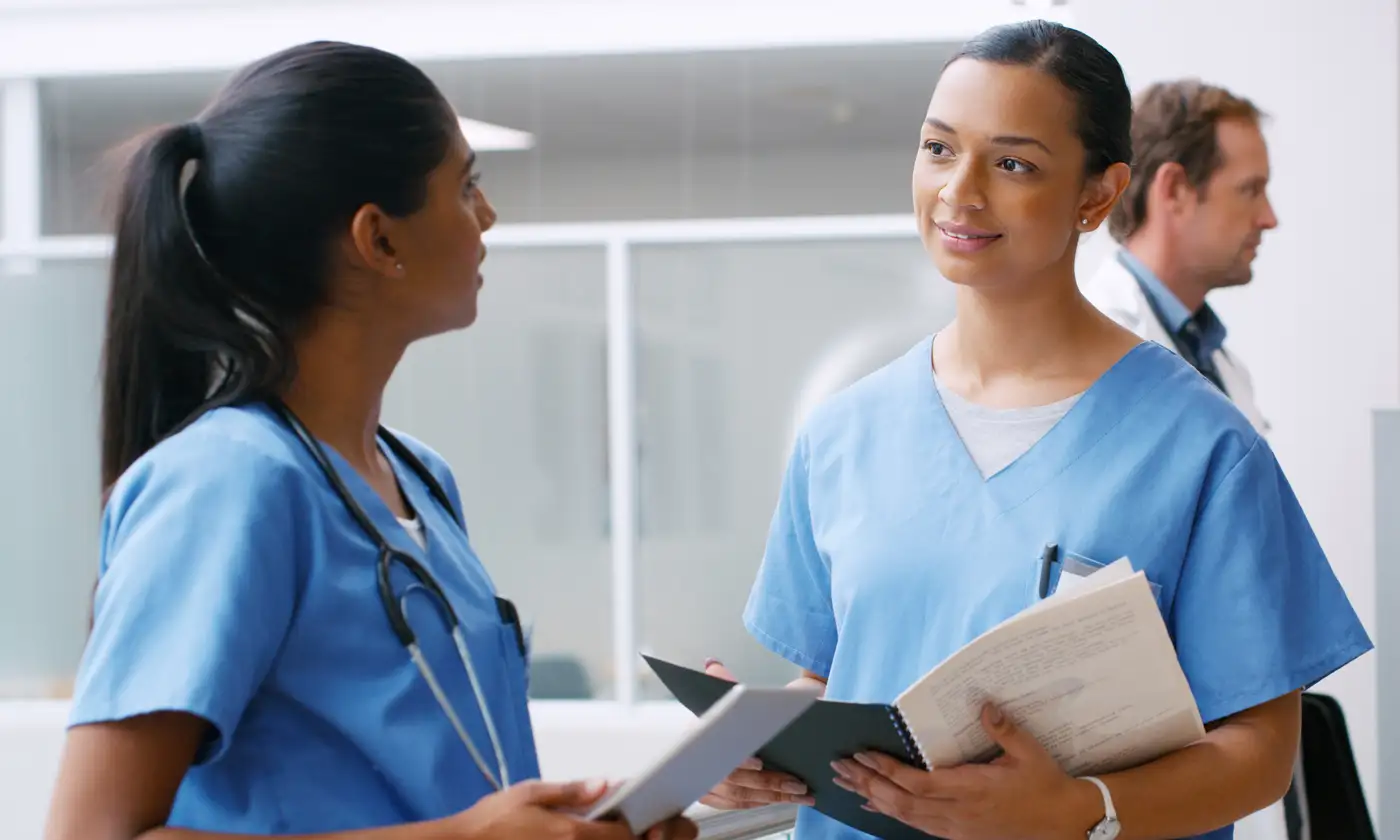 Two nurses in room talking to each other while holding medical folders
