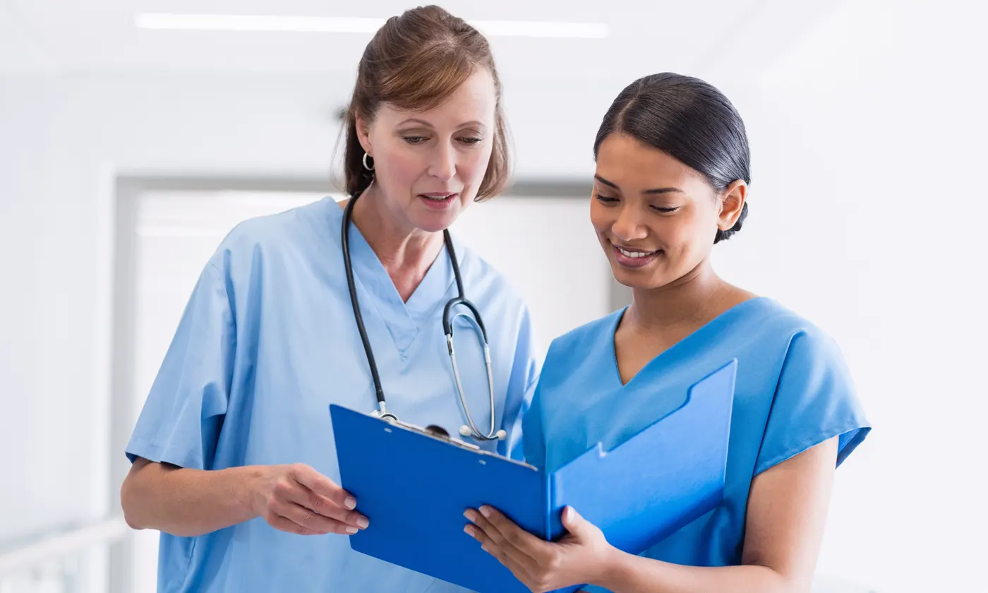 Two nurses in room talking to each other while holding medical folders