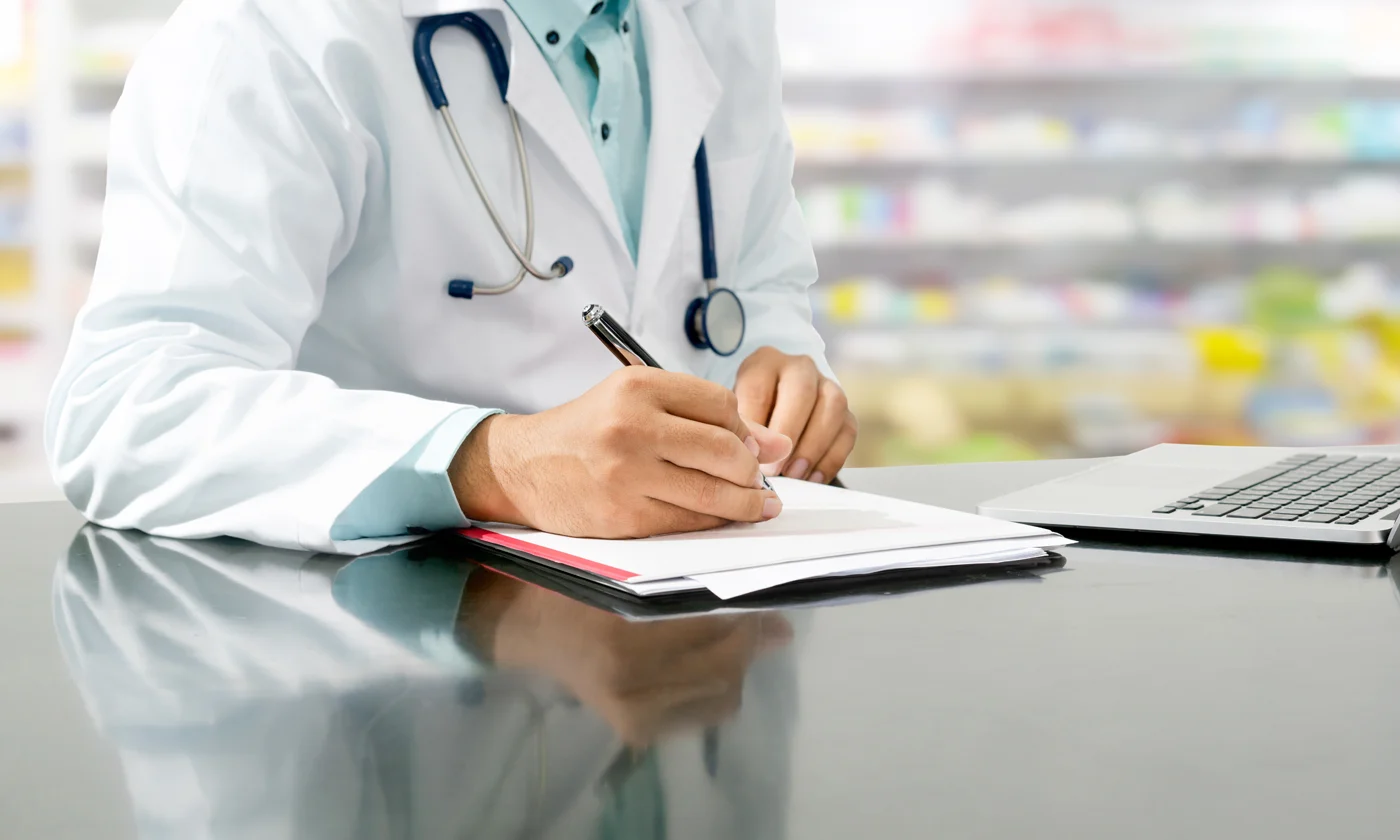 Pharmacist at desk writing notes in notebook in pharmacy 